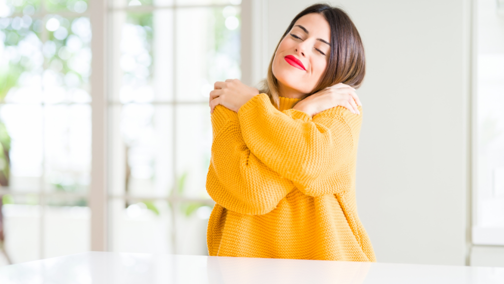 Women in orange sweater hugging herself as a form of self-care, the cure for Tension Myositis Syndrome